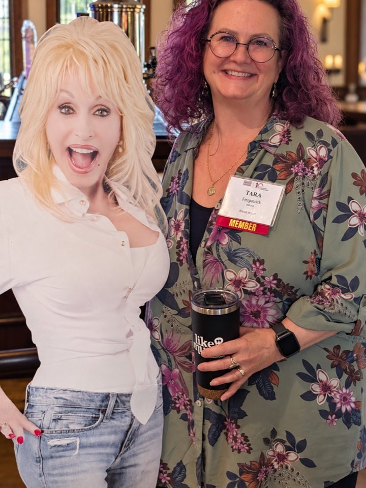 Tara Fitzpatrick smiling at a community event beside a Dolly Parton standee.